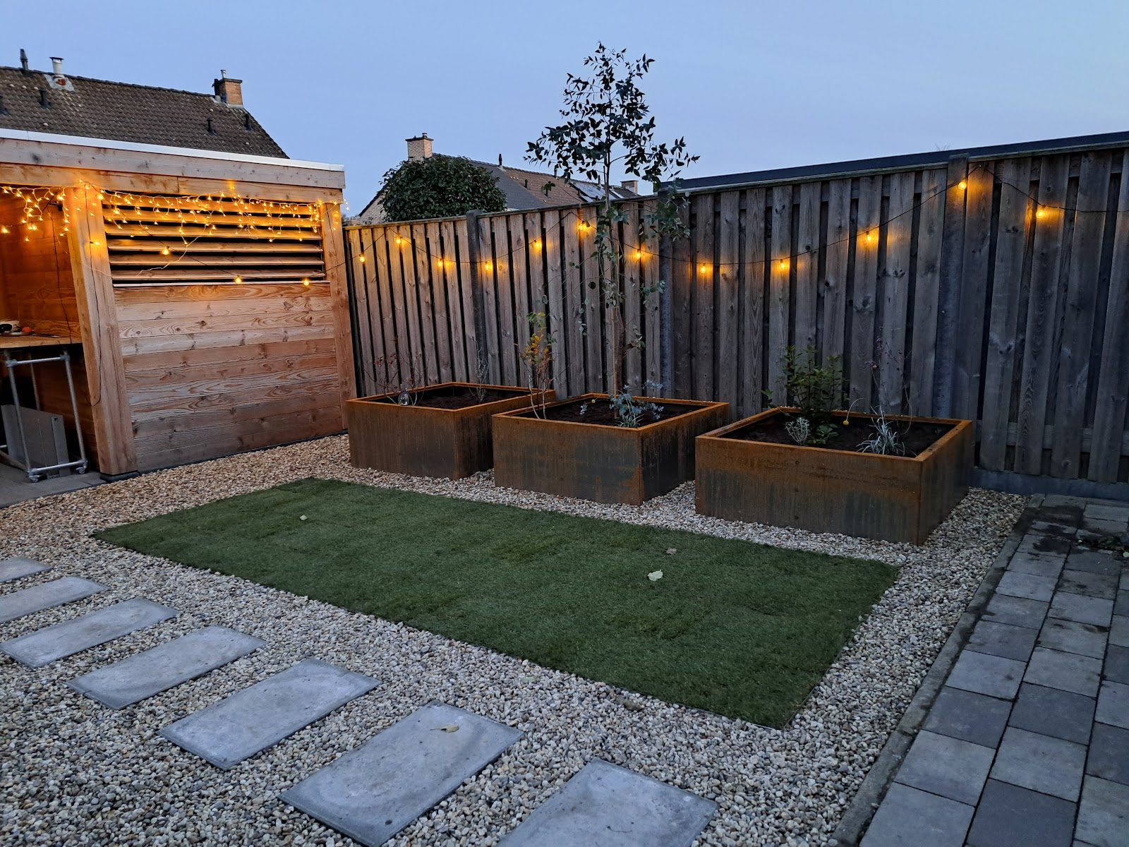 Garten mit Kies, Trittplatten, Rasenstück und Hochbeeten am Abend